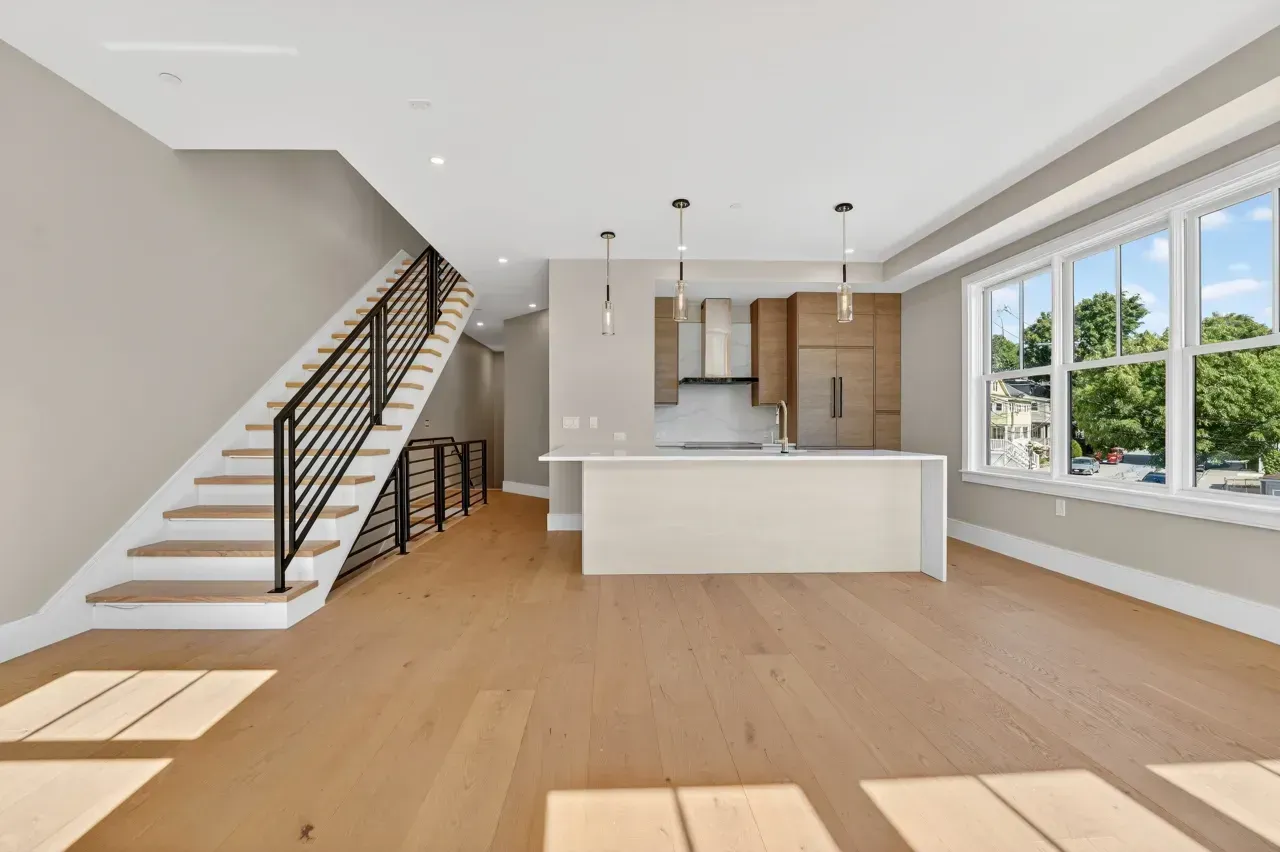 Bright modern open-plan kitchen and living area with white walls, wood floors, staircase, and large windows