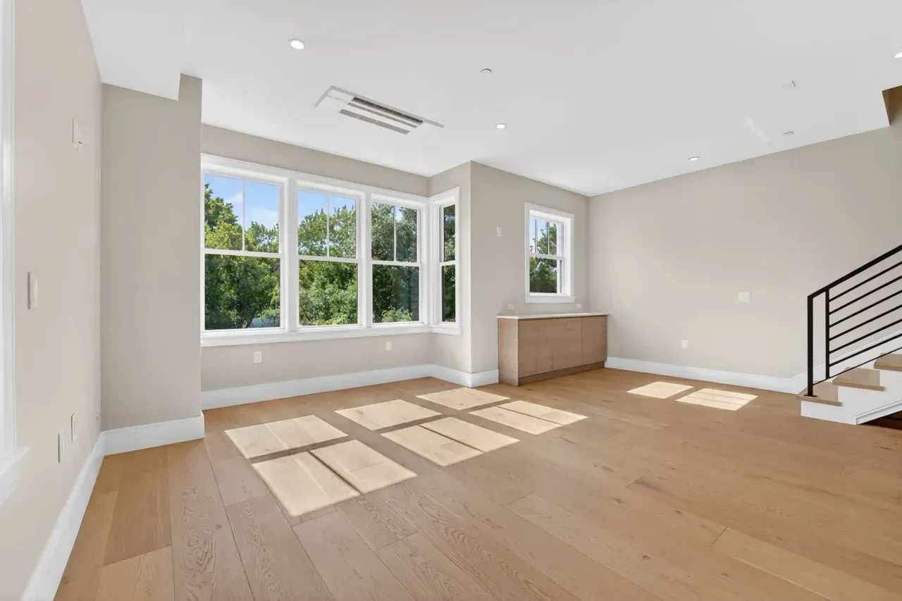 Bright empty room with wood floors, a window, built-in cabinet, and a staircase with black railings