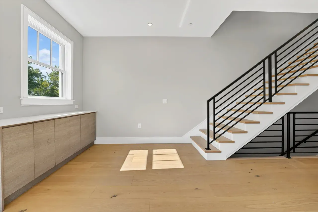 Bright modern room with wooden floor, built-in cabinet, window, and black-railed staircase