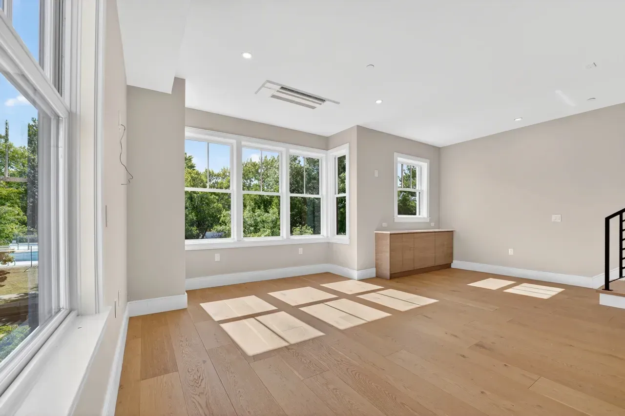 Bright empty living room with large windows, light wood floors, and beige walls
