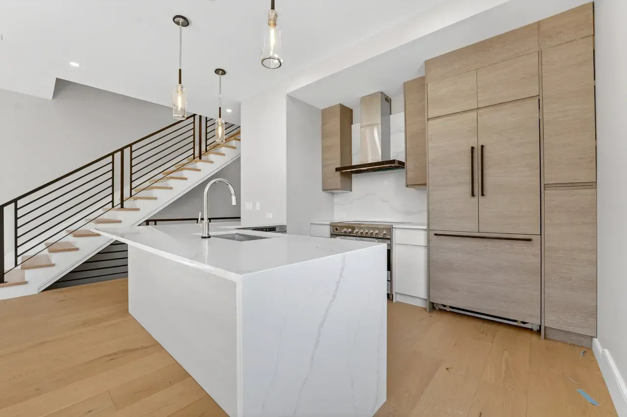 Modern kitchen with white island, light wood cabinets, and staircase in the background