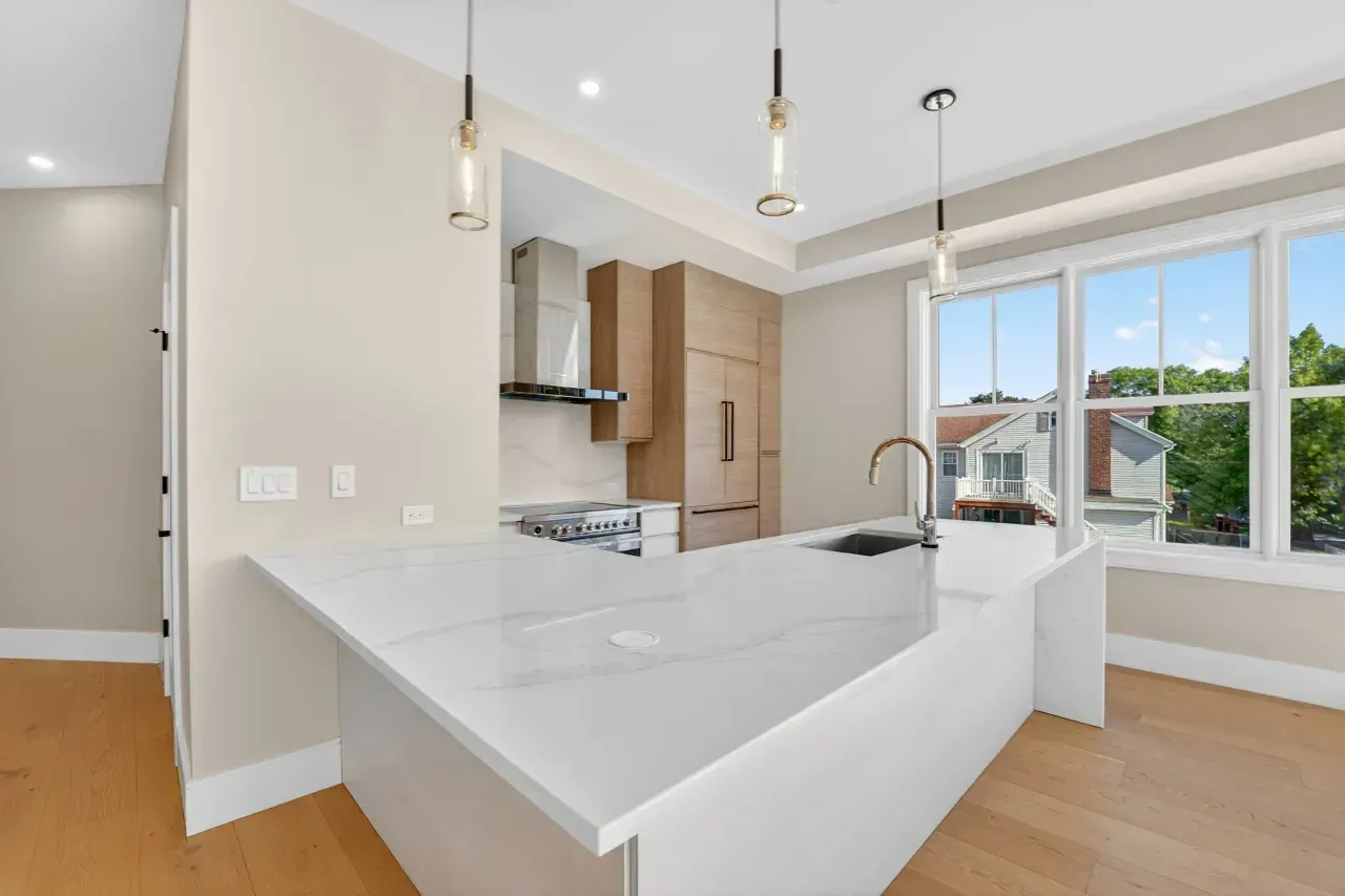 Bright modern kitchen with white island, pendant lights, wood cabinets, and large windows