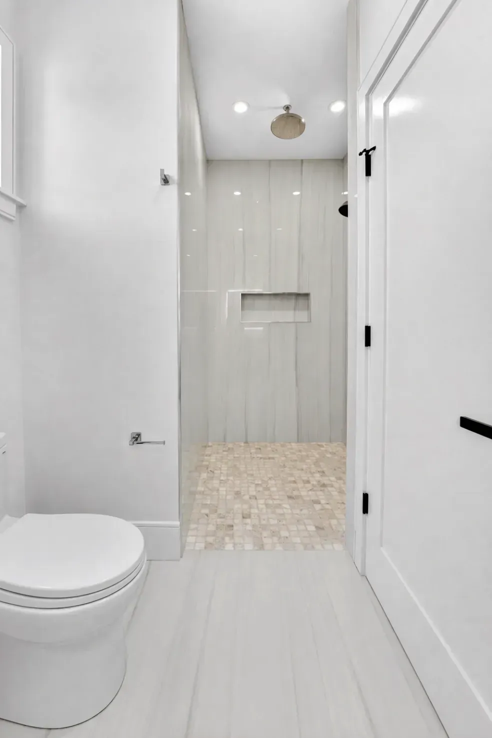 White bathroom with toilet, tiled shower, and bright white walls and floor
