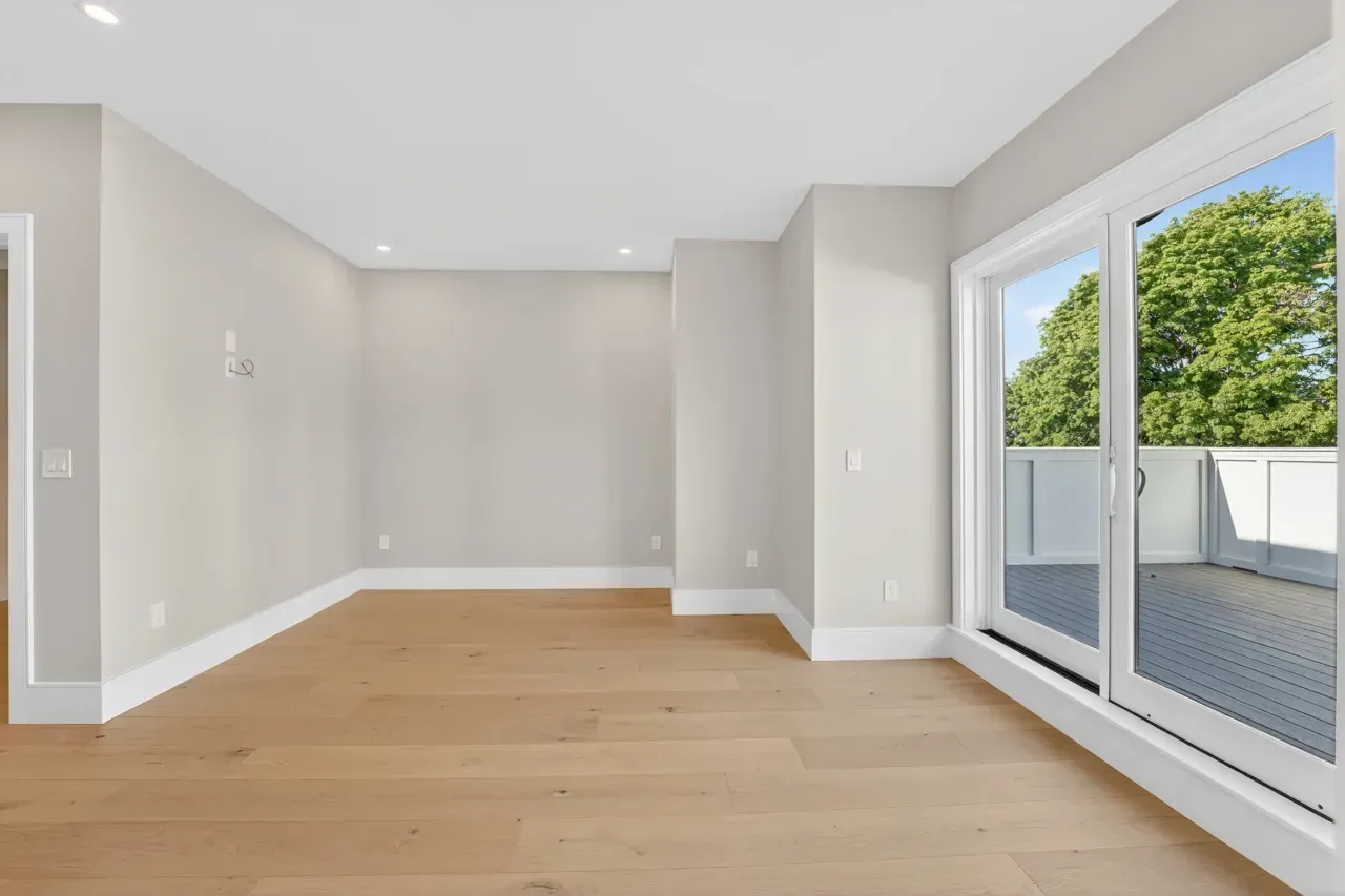 Empty modern room with light wood floors, gray walls, and large sliding glass doors opening to a patio
