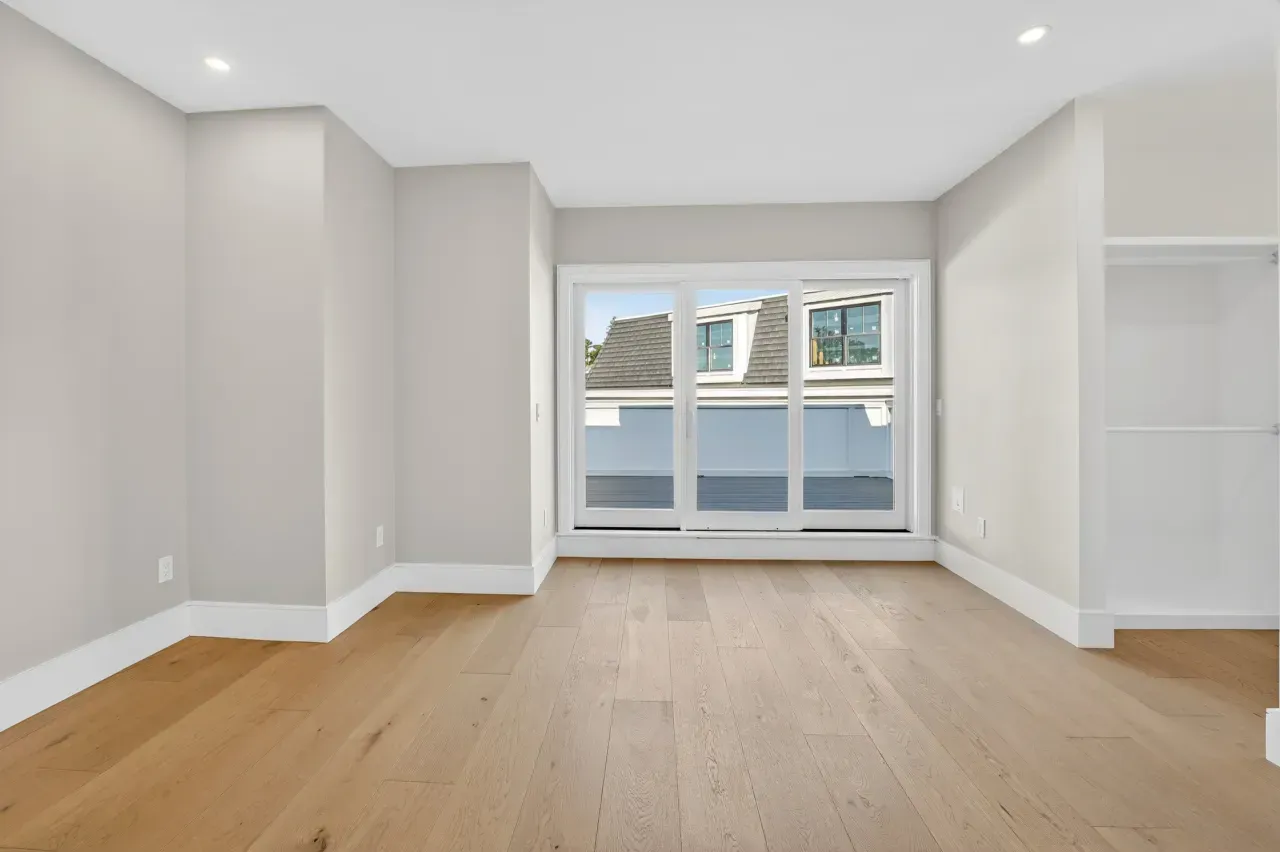 Bright empty modern room with light wood floors and large windows leading to a balcony