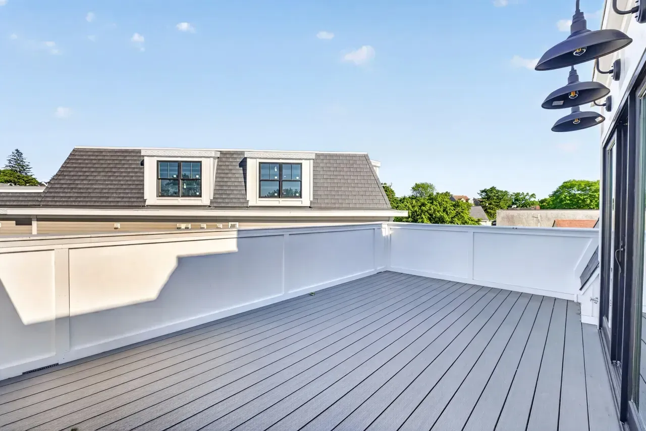 Spacious white rooftop deck with gray flooring and neighboring houses under a blue sky