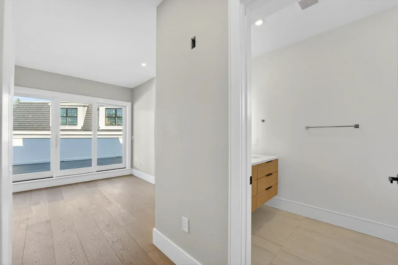 Bright empty apartment with light wood floors, white walls, and sliding glass doors to a balcony