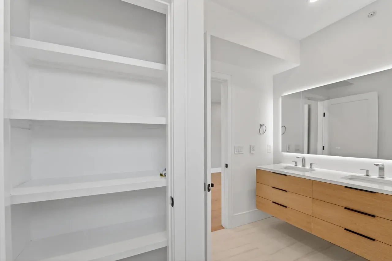 Bright white bathroom with built-in shelves, long wood vanity, and large mirror