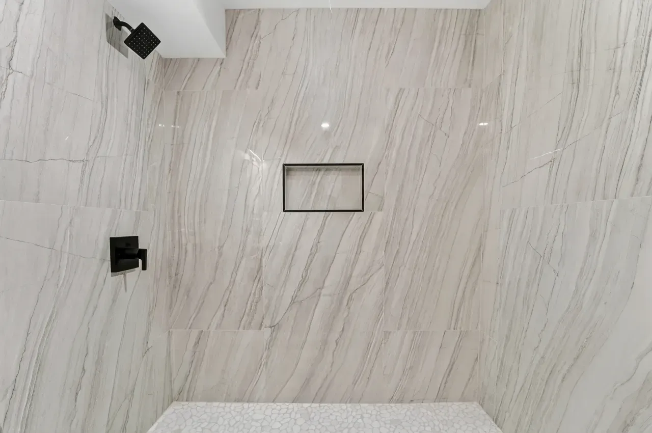 White marble-tiled shower wall with a small recessed niche and black fixtures