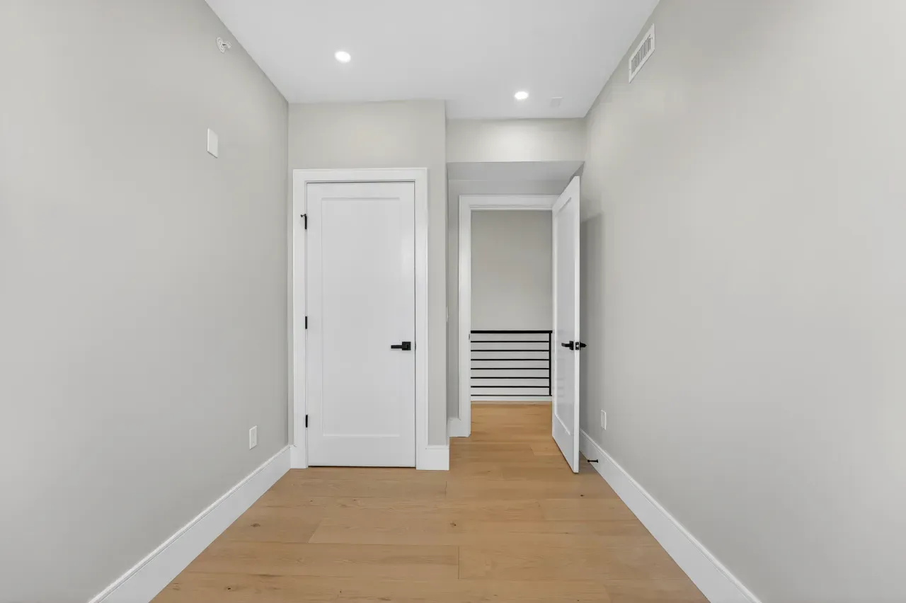 Empty white hallway with light wood floor, open door, and a closet at the end