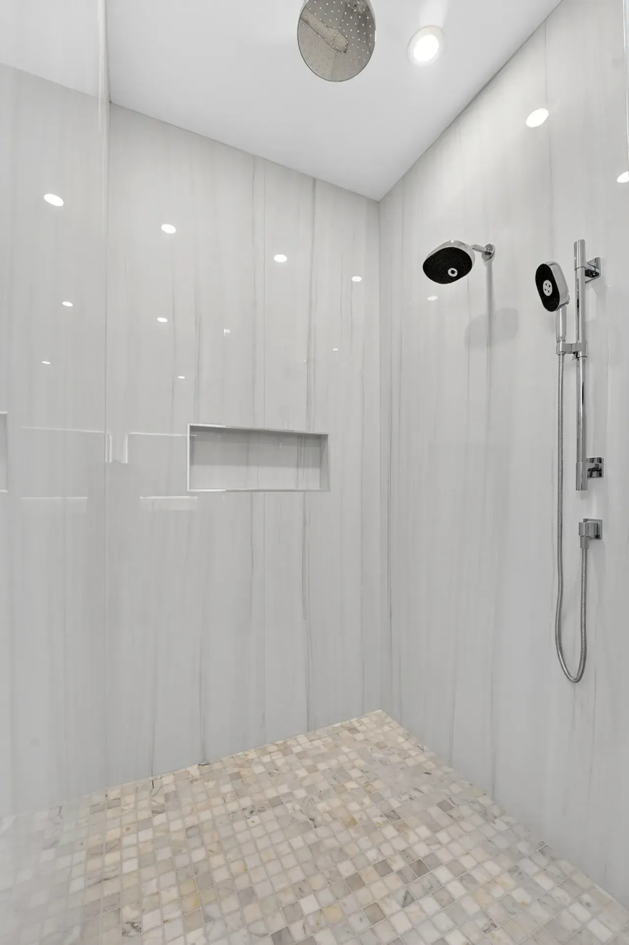 Modern shower stall with light gray tile walls, mosaic floor, showerhead, and handheld sprayer