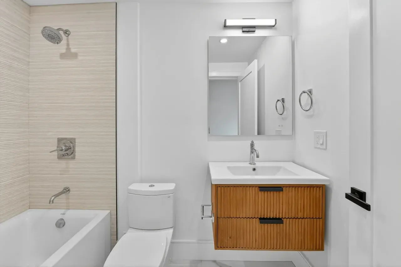 Modern bathroom with a tub-shower, toilet, and wood vanity with mirror and sink