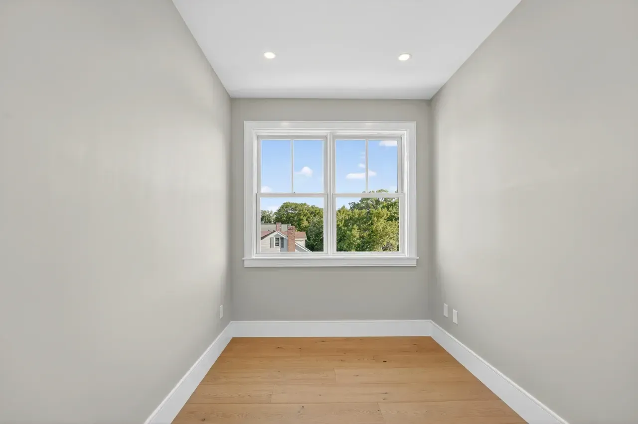 Empty gray room with hardwood floor and a window overlooking trees and houses