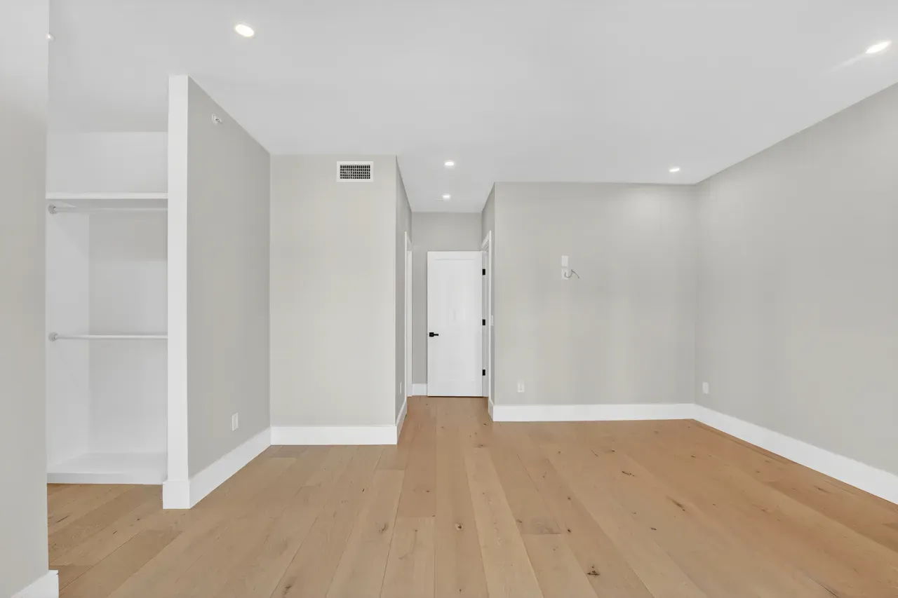 Empty modern room with light wood floors, gray walls, white trim, and recessed ceiling lights