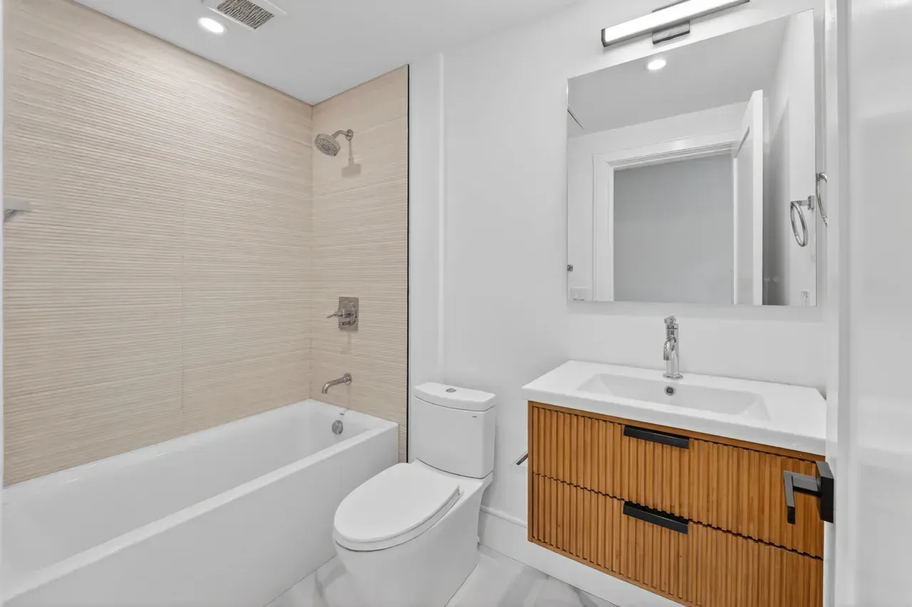 Modern white bathroom with bathtub, toilet, vanity, and mirror on tiled walls