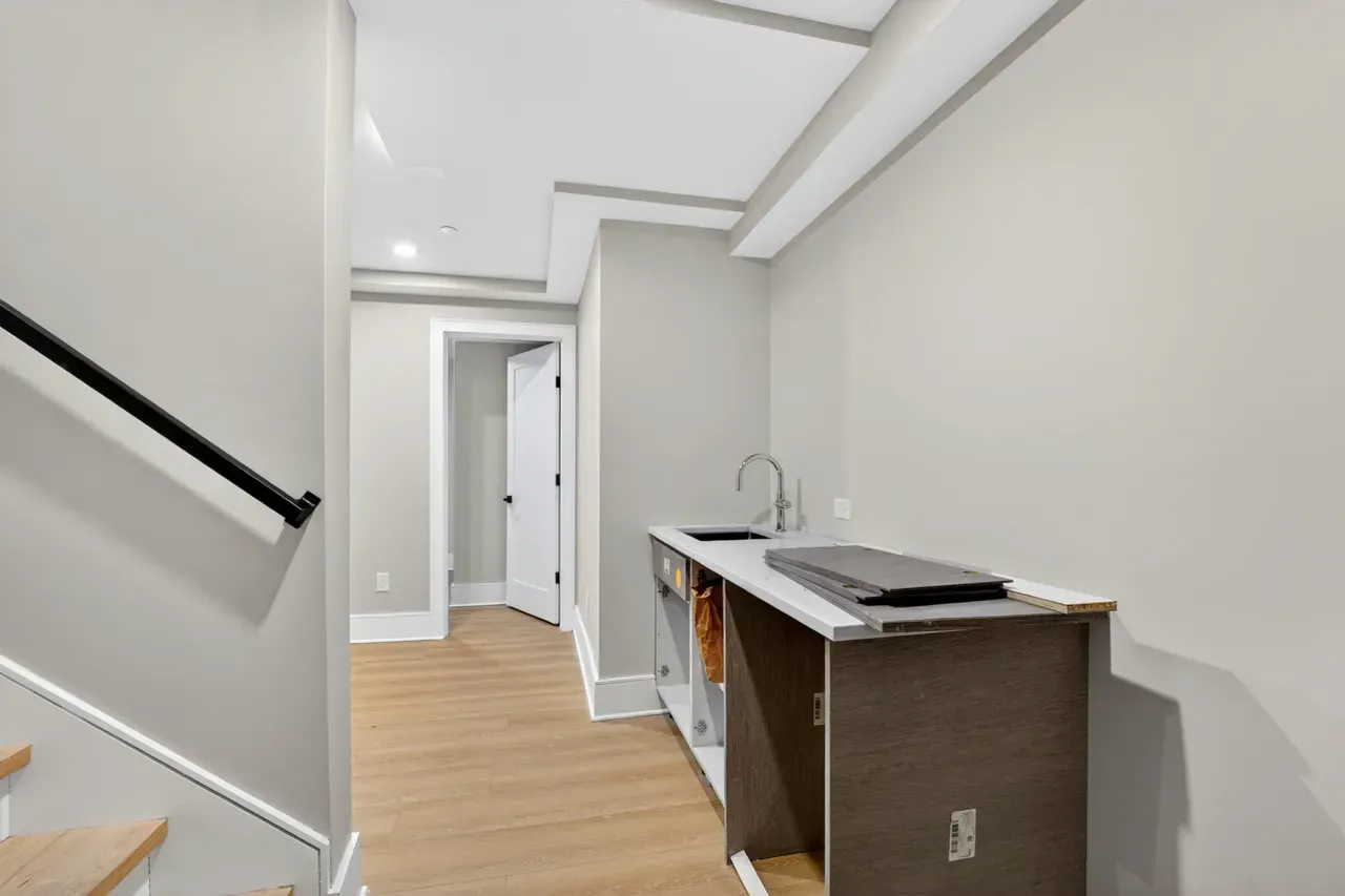 Bright hallway with wood floor, white walls, and a small countertop with a laptop on the right