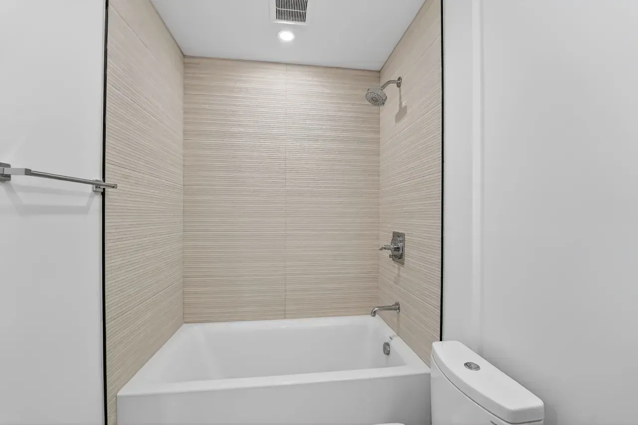 Small tiled bathroom with a white bathtub and shower fixtures
