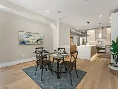 Dining area with glass table and black chairs on a blue rug in a bright modern open-plan room