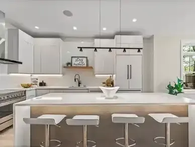Modern white kitchen with island, bar stools, pendant lights, and stainless steel refrigerator