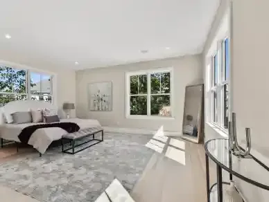 Bright, modern bedroom with large windows, gray rug, upholstered bed, and a glass side table