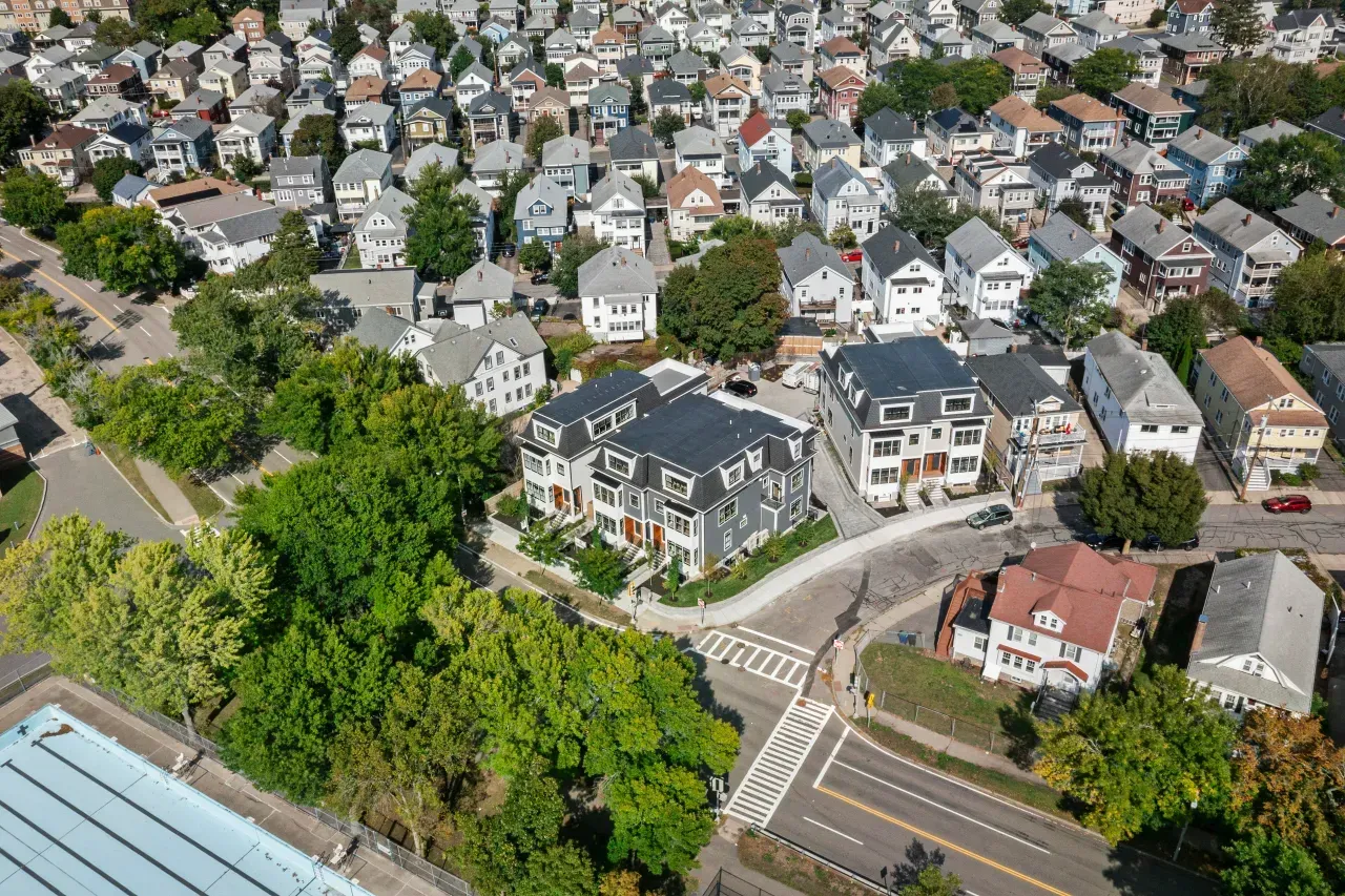 Aerial view of a dense neighborhood with houses, trees, and curving streets near a road intersection