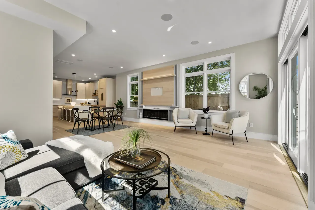 Bright open-plan living room with gray sectional, dining area, large windows, and light wood floors