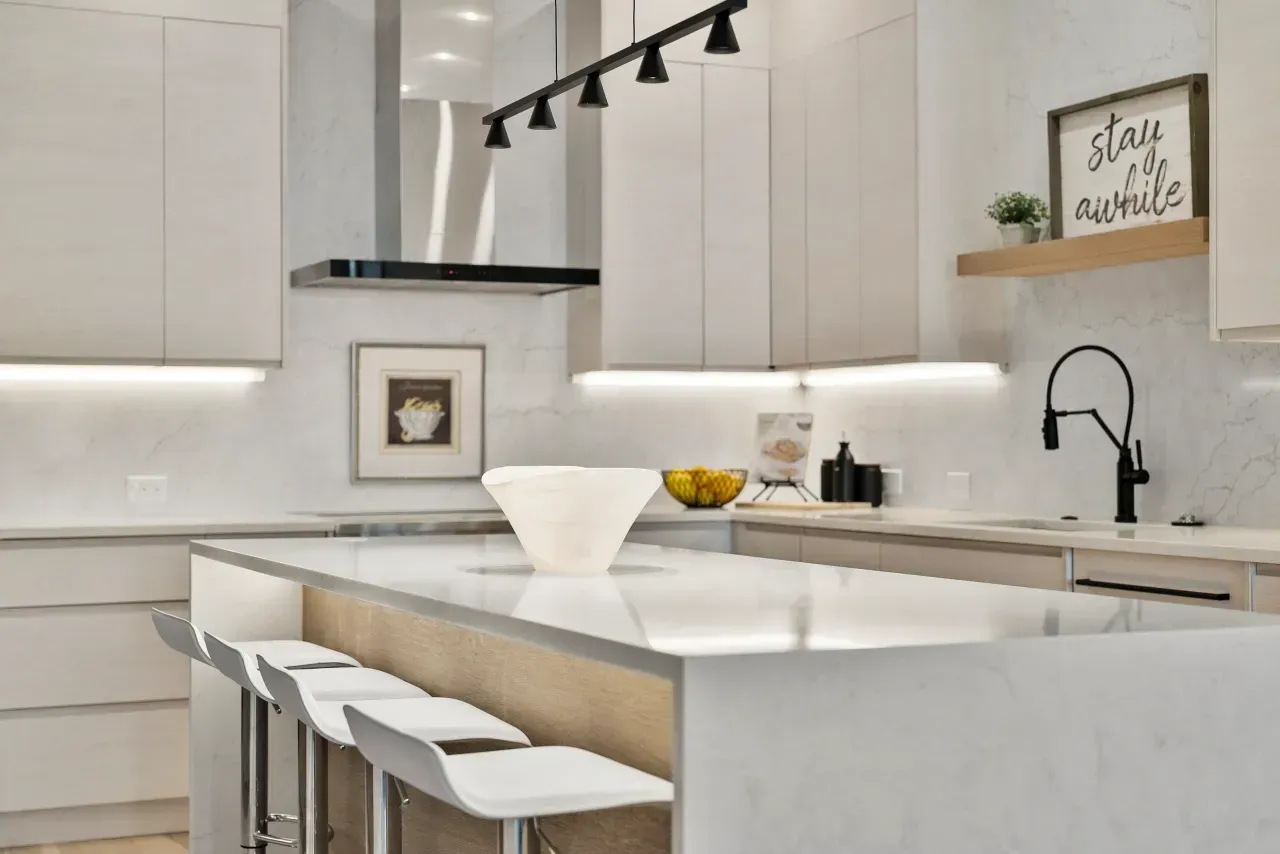 Modern white kitchen with island, bar stools, black pendant lights, and a sink by a window