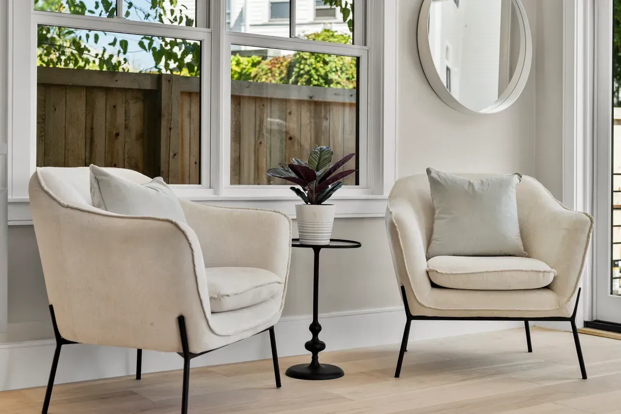 Two beige armchairs with a small side table in a bright living room by a window