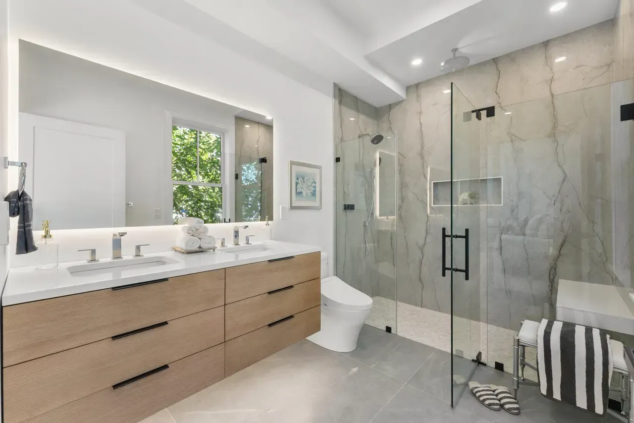 Modern bathroom with double vanity, large mirror, and glass-enclosed marble shower