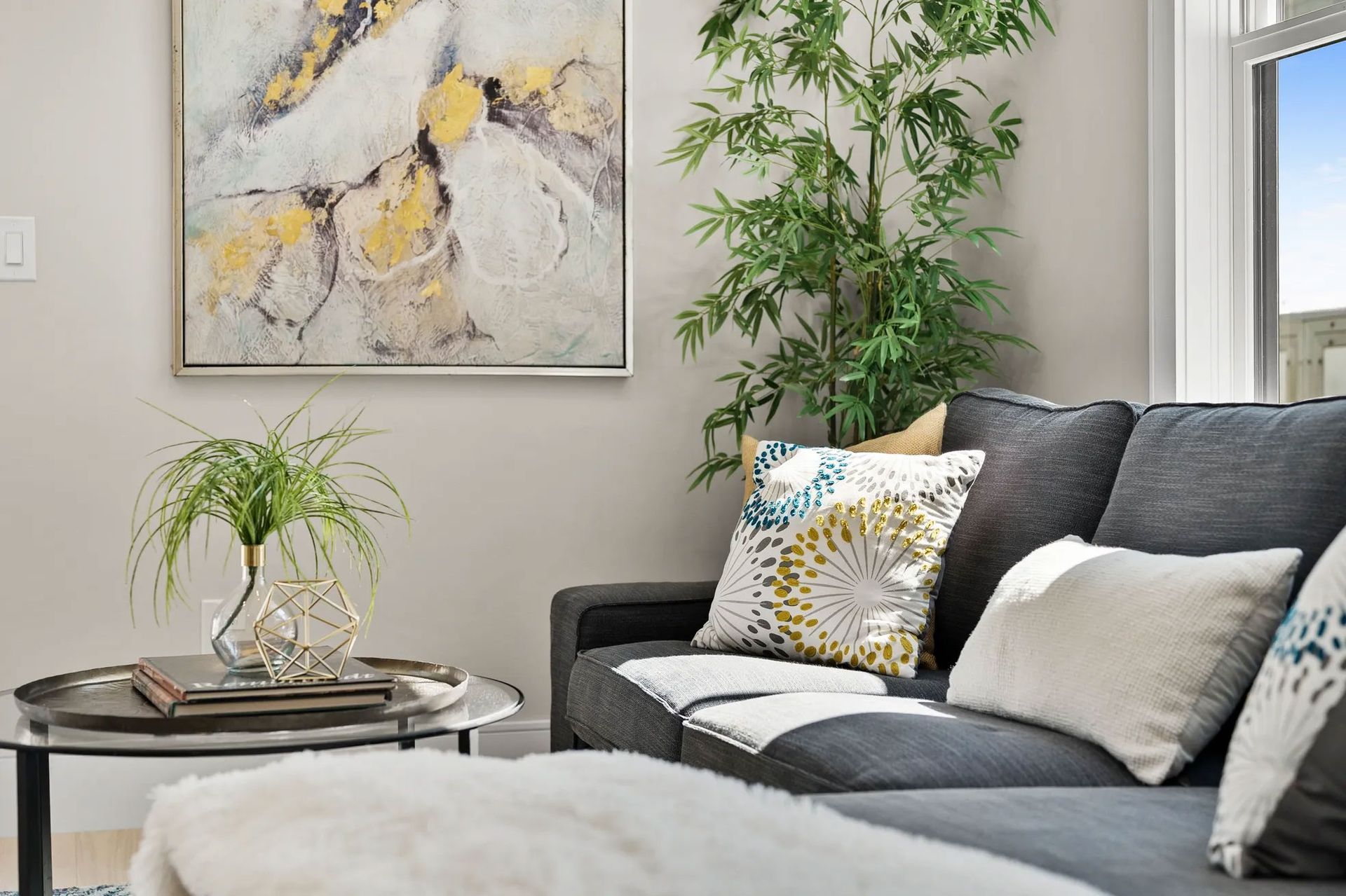 Living room with gray sofa, art, bamboo plant, and coffee table.