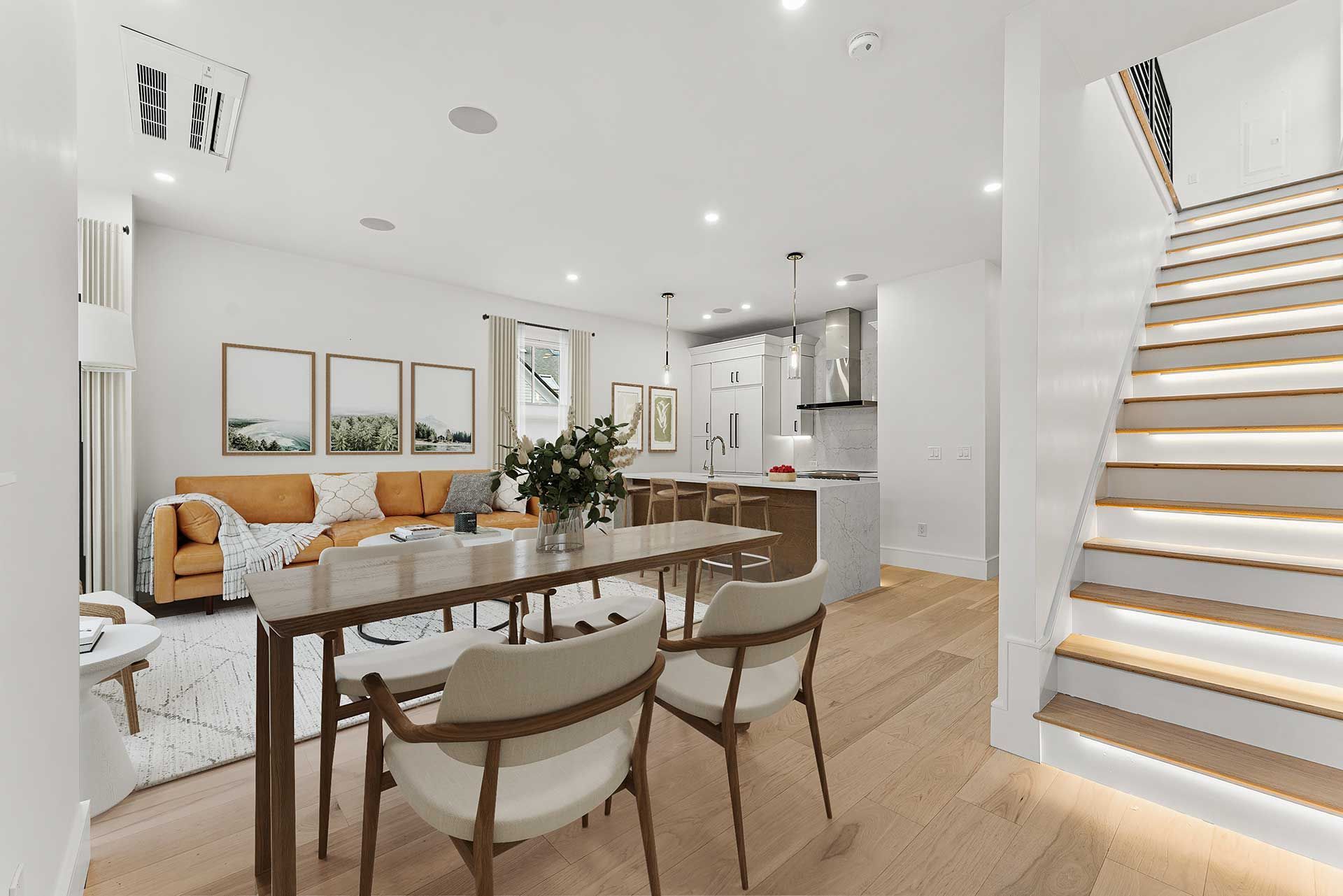 Bright modern dining and kitchen area with light wooden floors, white walls, and a staircase.