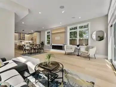 Spacious open-concept living area with light wood floors, a modern fireplace, and a connected kitchen.