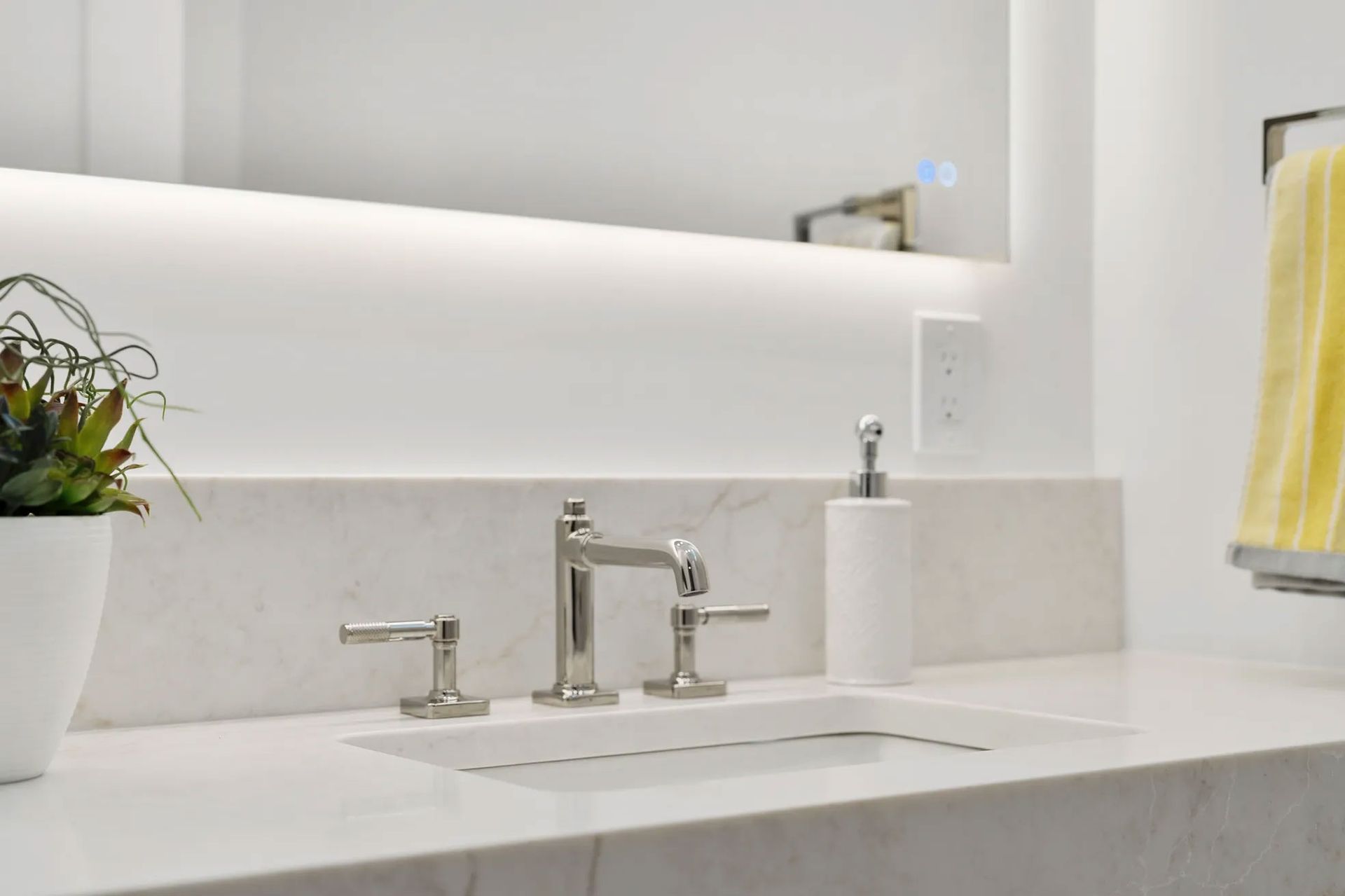 Modern white bathroom sink with chrome faucet, soap dispenser, and a yellow towel.