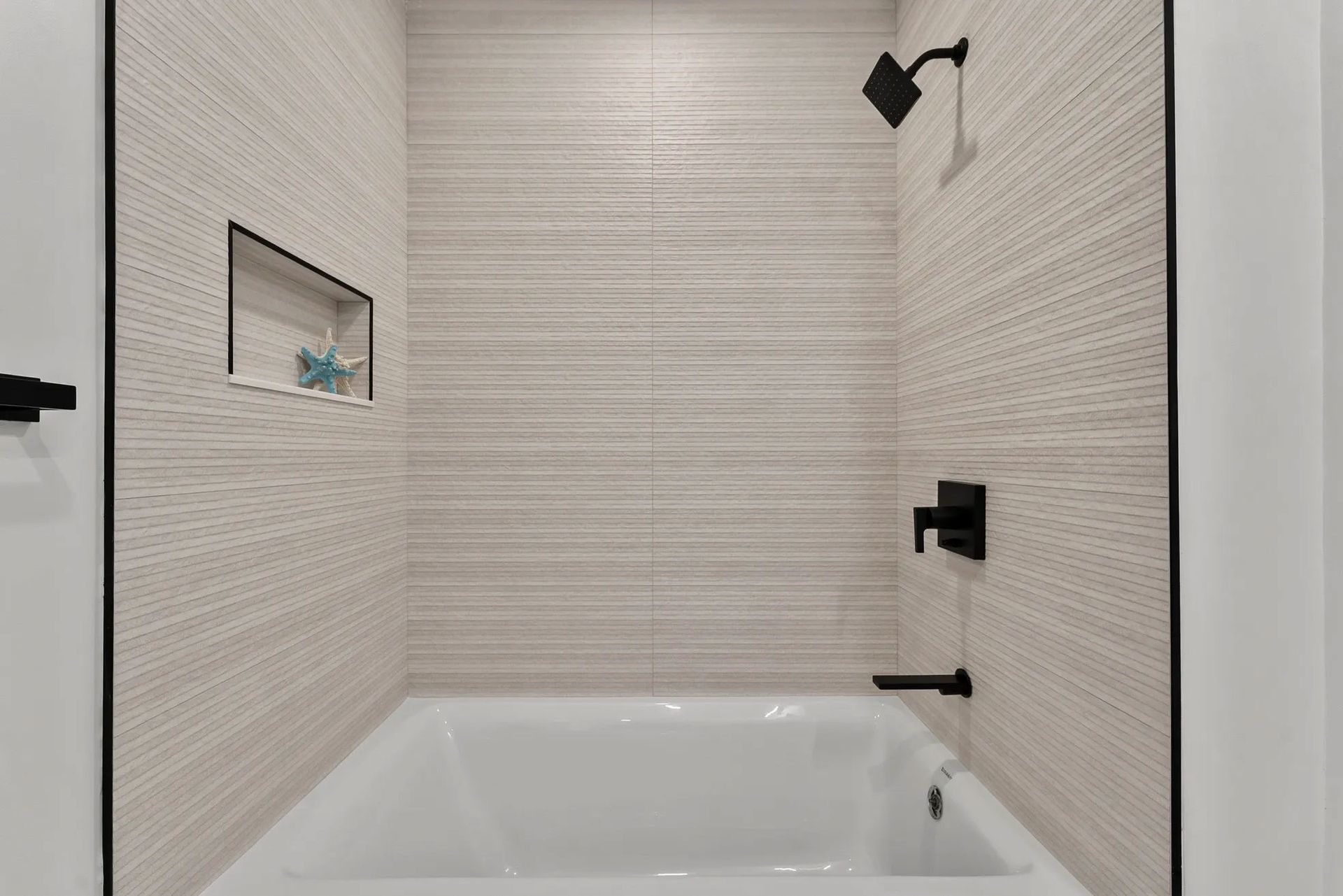 Modern bathroom shower with white tiled walls, black fixtures, and a recessed shelf.