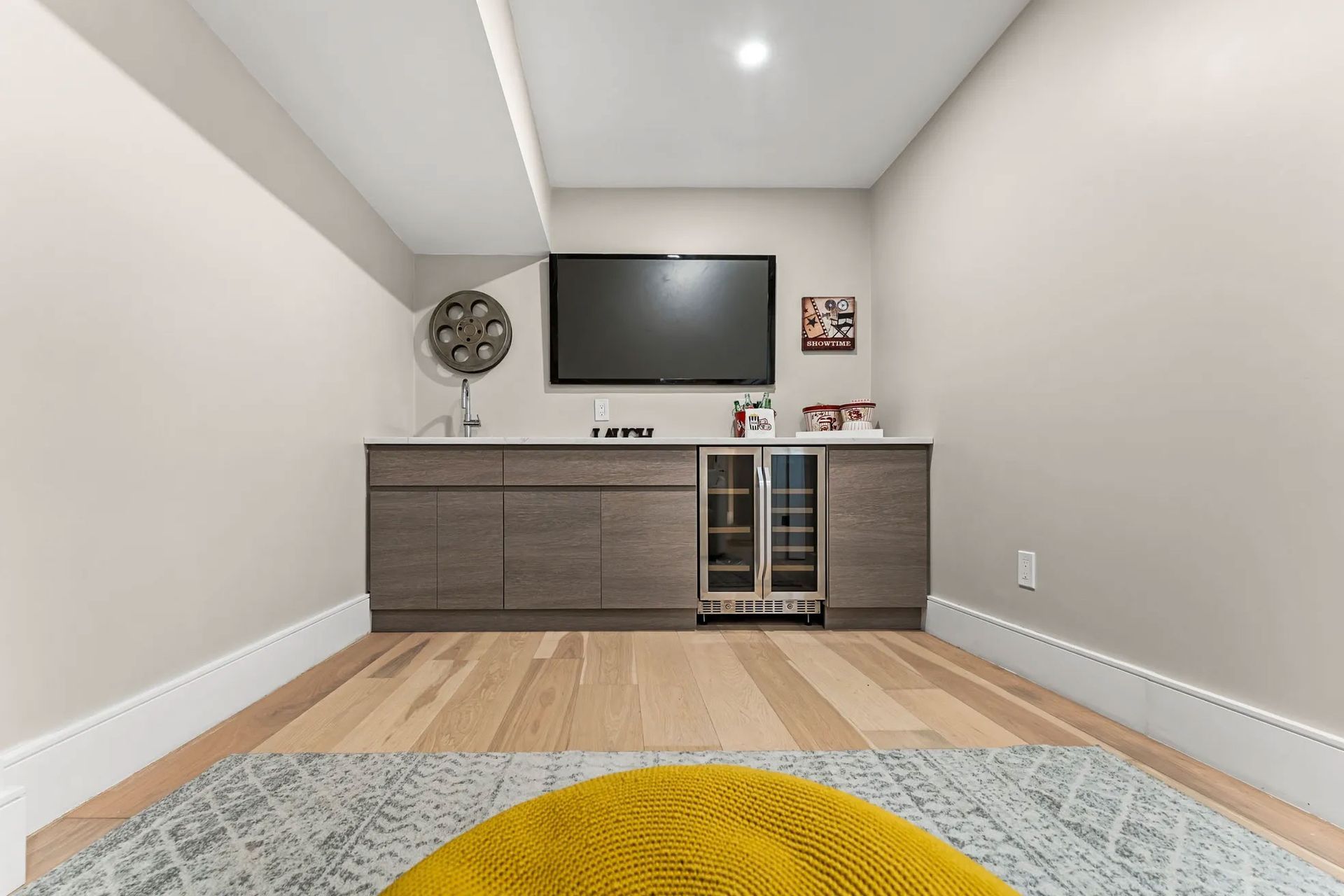 Small entertainment room with TV, bar cabinet, fan, and light wood flooring.