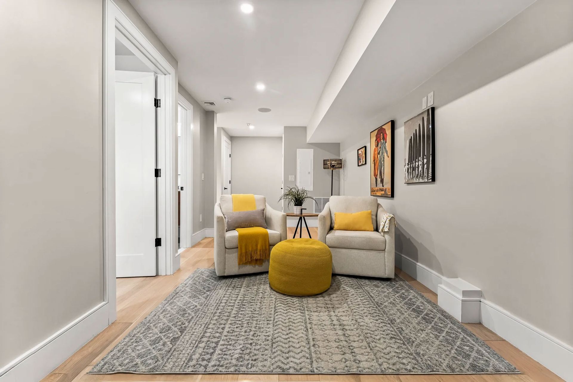 Cozy basement seating area with two armchairs, a yellow ottoman, and a patterned rug.