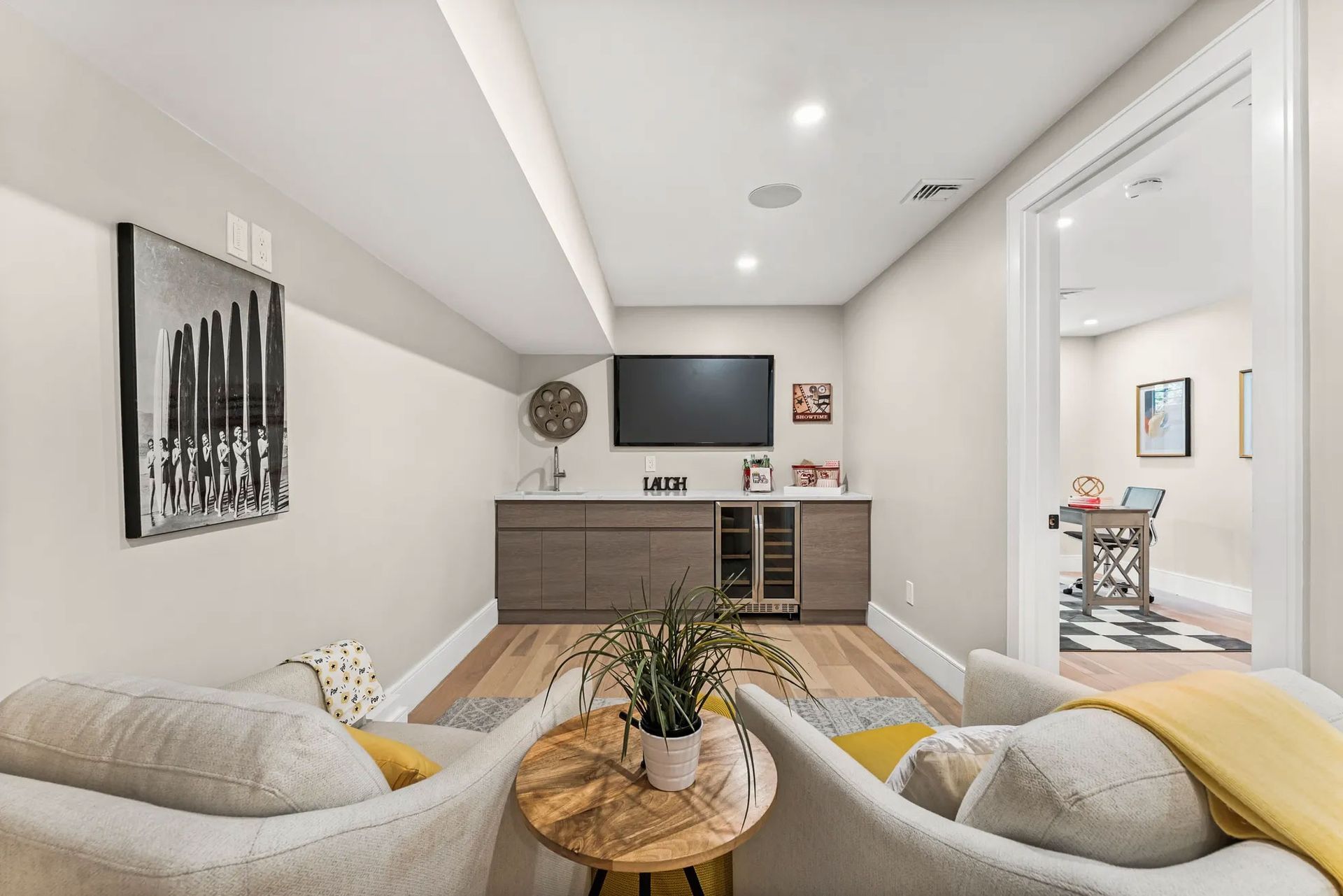 Cozy basement living area with two armchairs, a TV, and a bar area. A door leads to another room.
