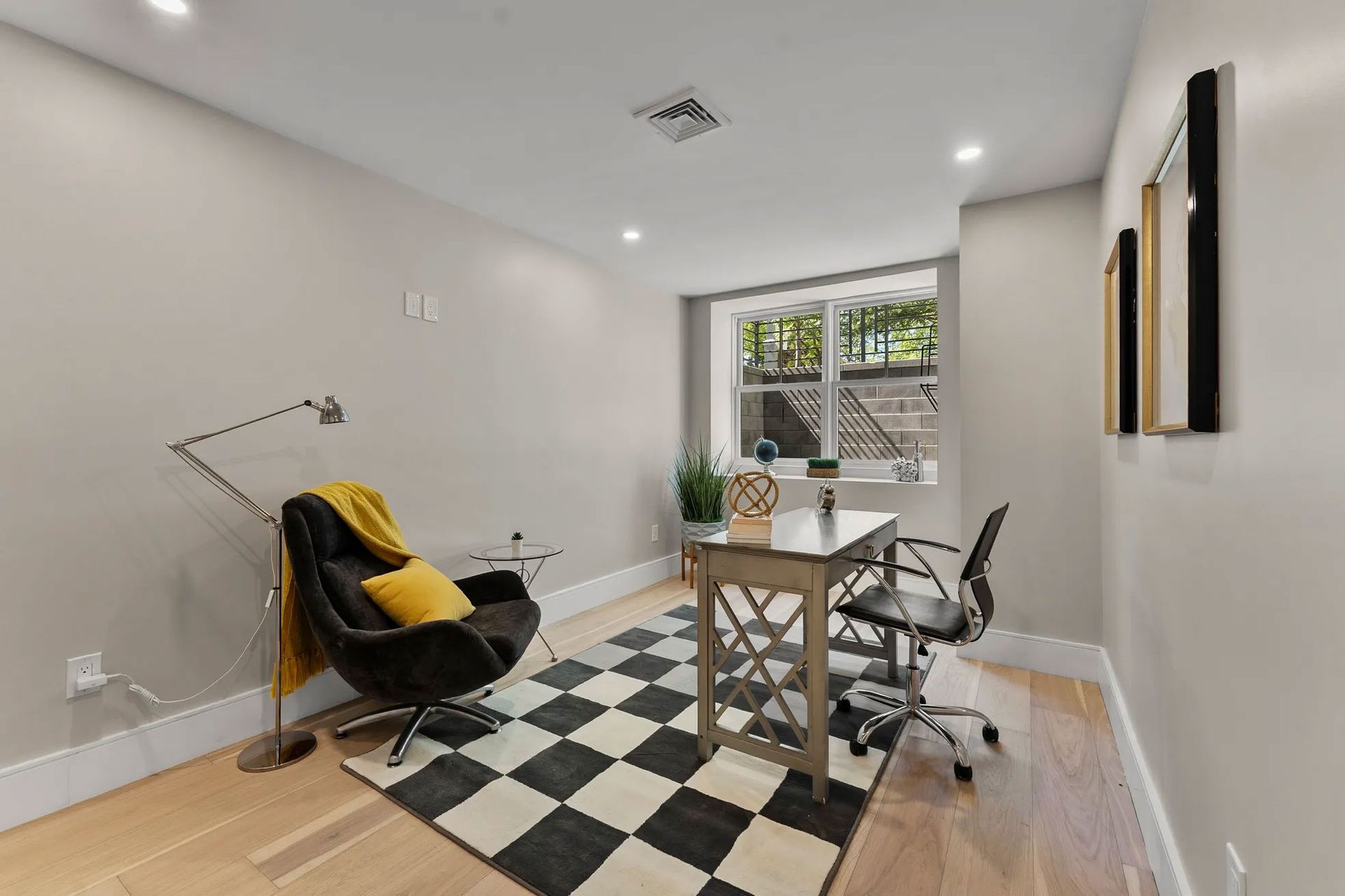 Home office with a desk, chair, accent chair, checkered rug, and window.
