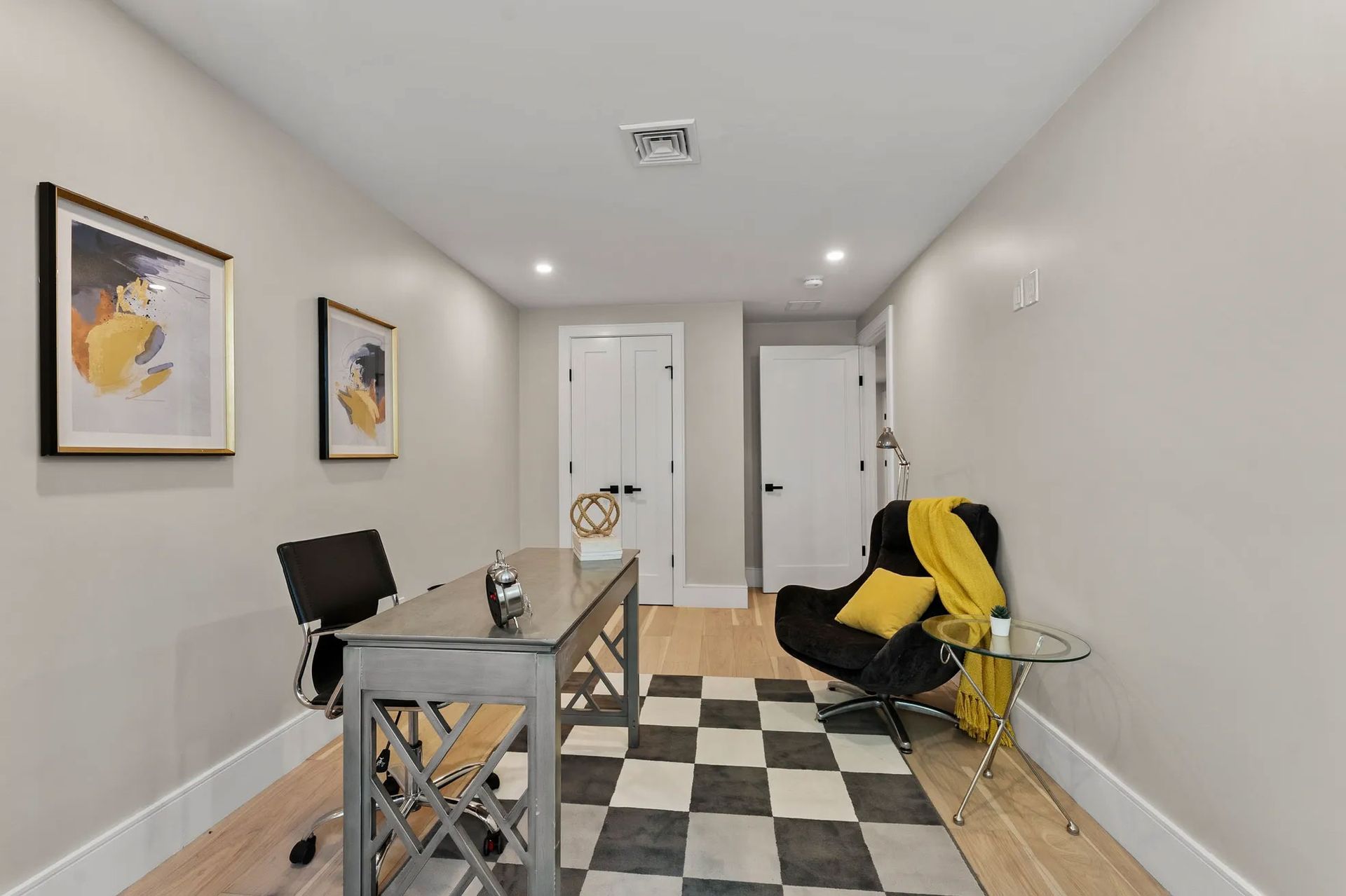 Home office with a desk, black chair, black and white checkered rug, and artwork.