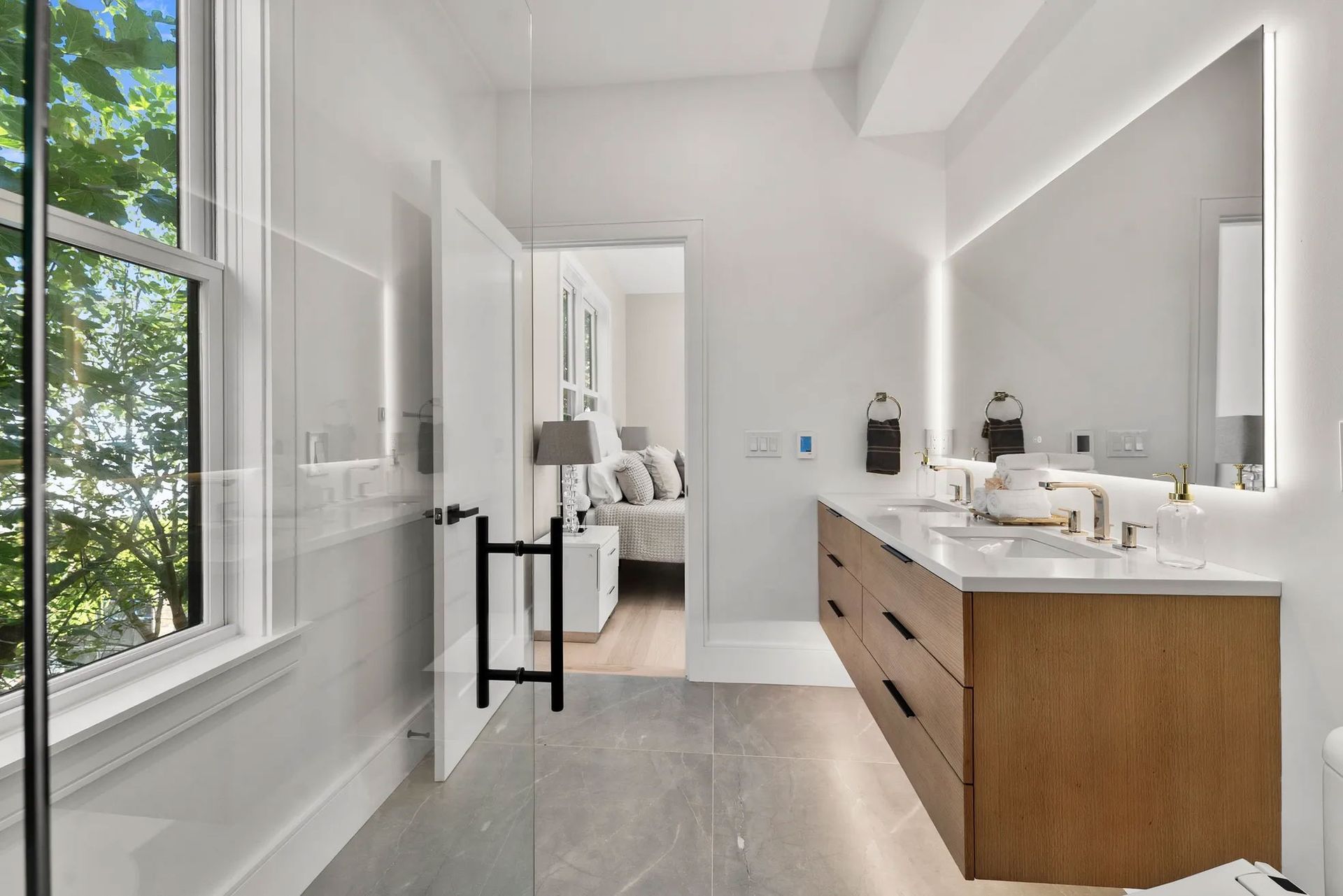 Modern bathroom with a wooden vanity, large mirror, and open door to a bedroom.