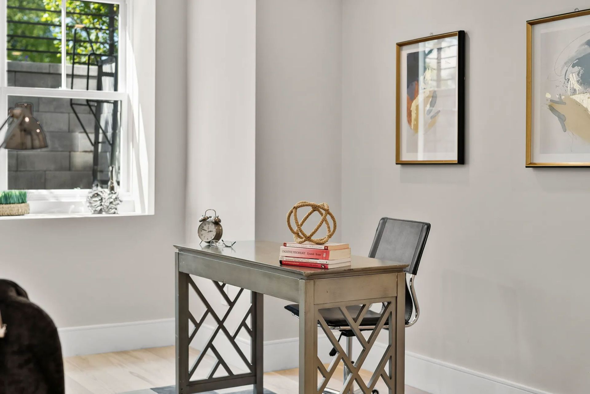Desk in home office with chair, decor, window, and artwork.