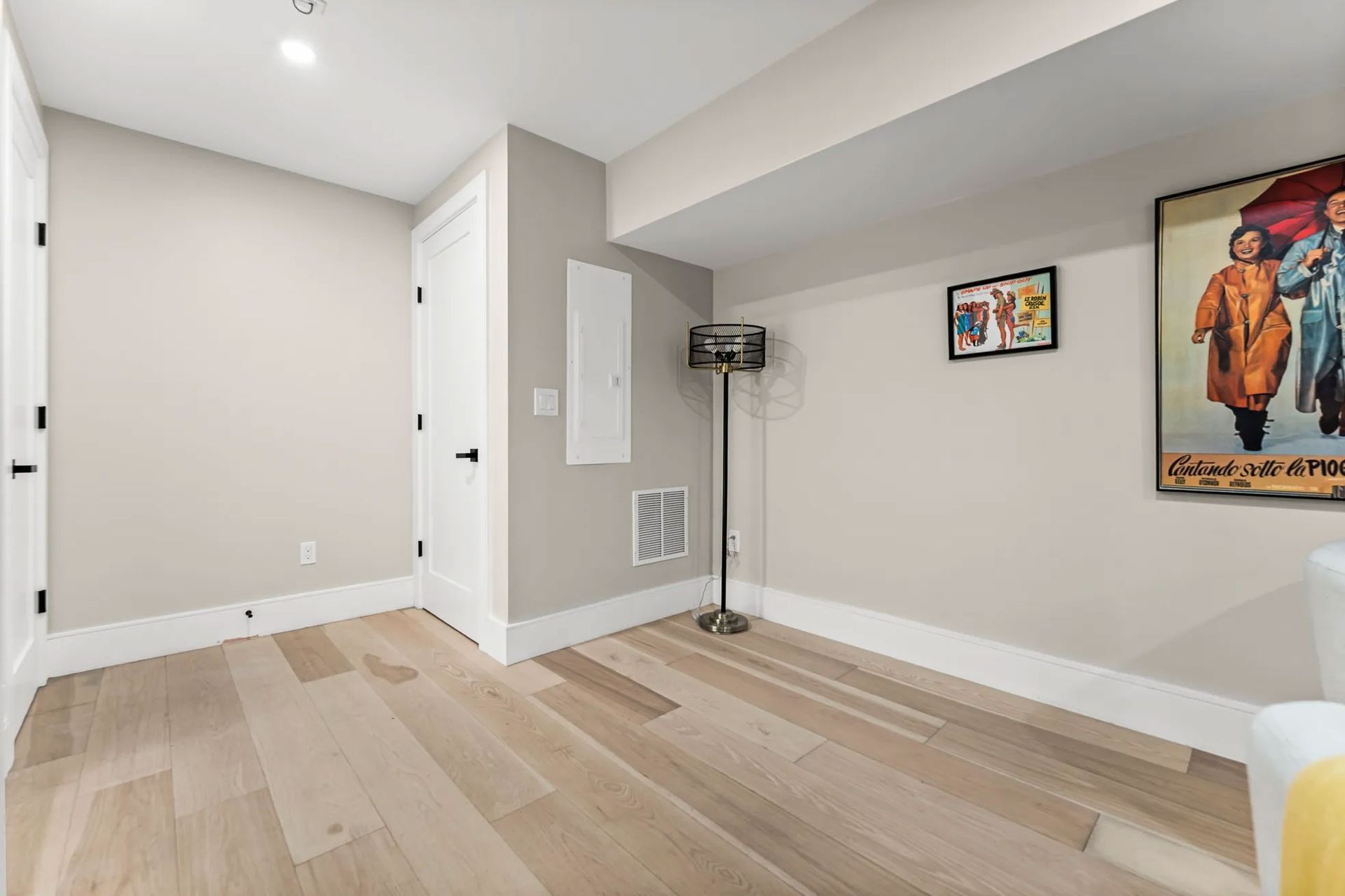 Empty room with light wood flooring, white trim, and neutral walls. A floor lamp and artwork are present.