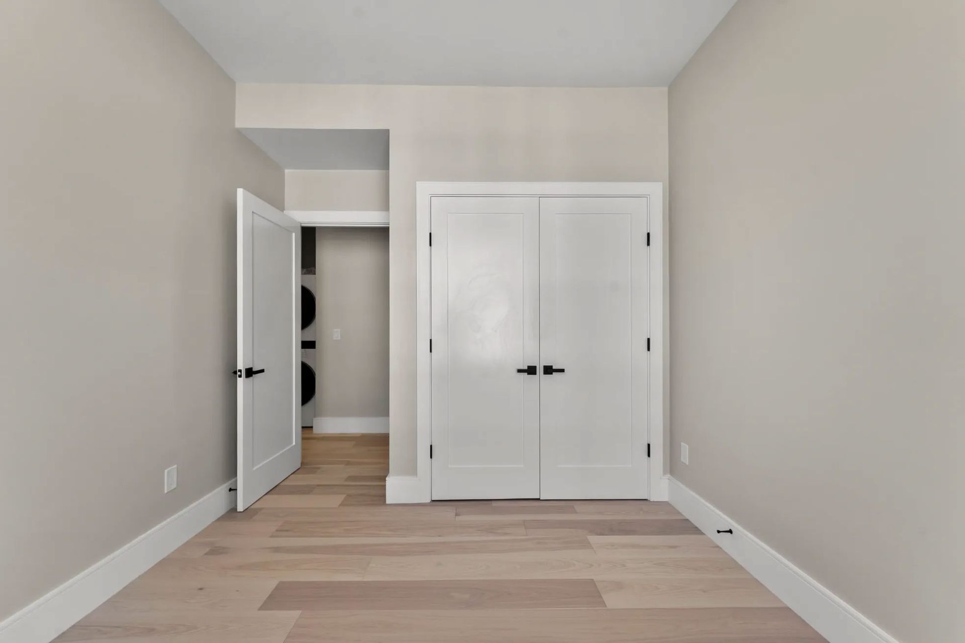 Empty room with light wood floors, white trim, and white doors. A closet is on the left.