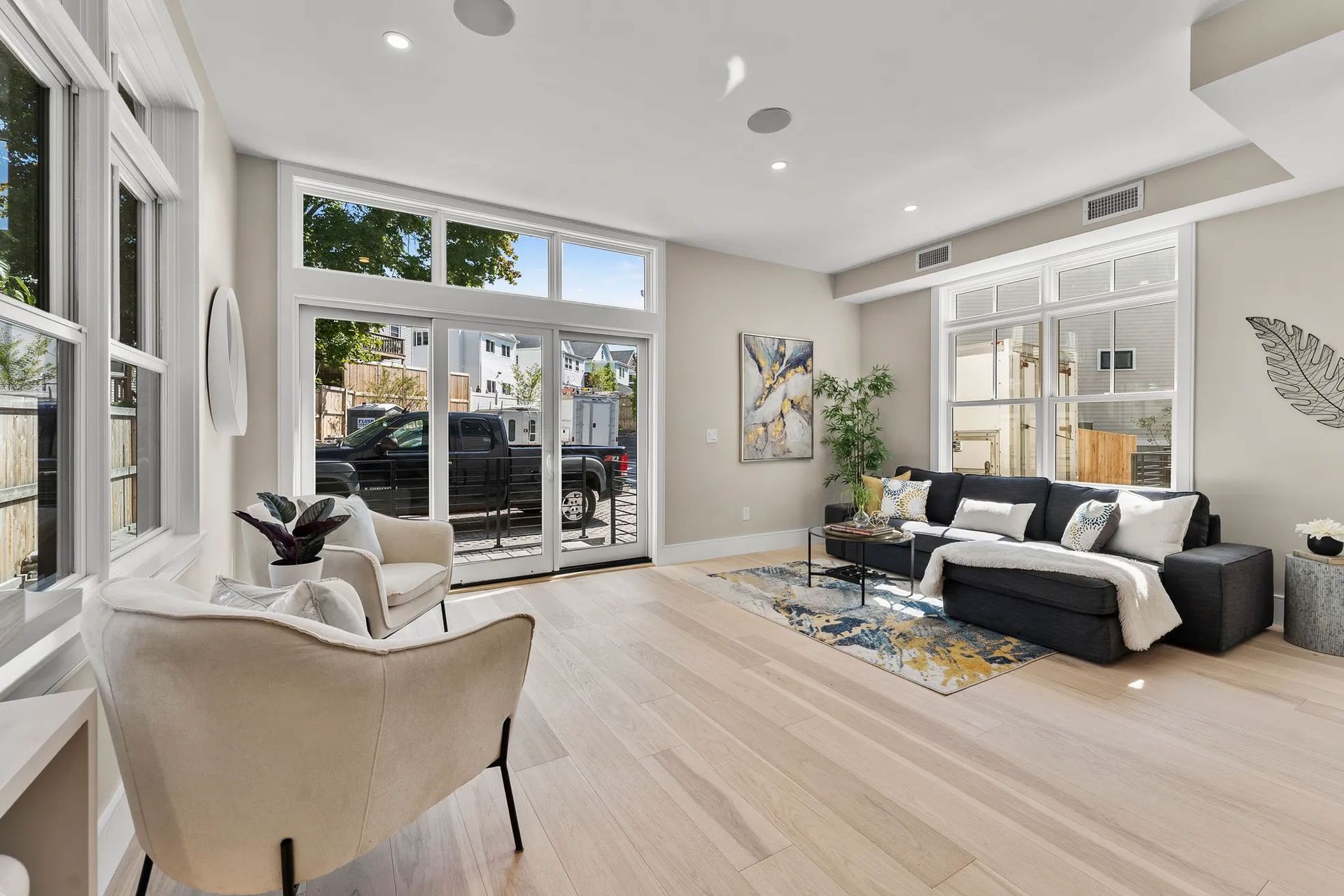 Spacious living room with light wood floors, large windows, and modern furniture.