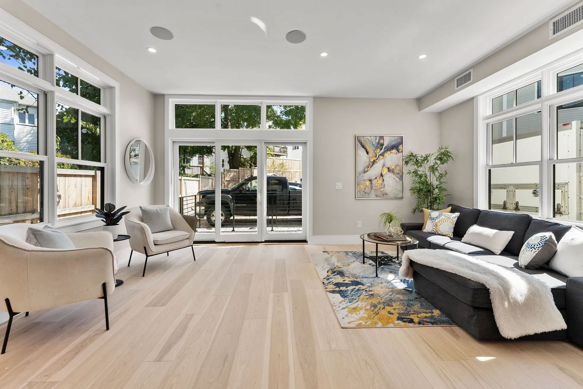 Bright, modern living room with light wood floors, large windows, and a dark gray sectional sofa.