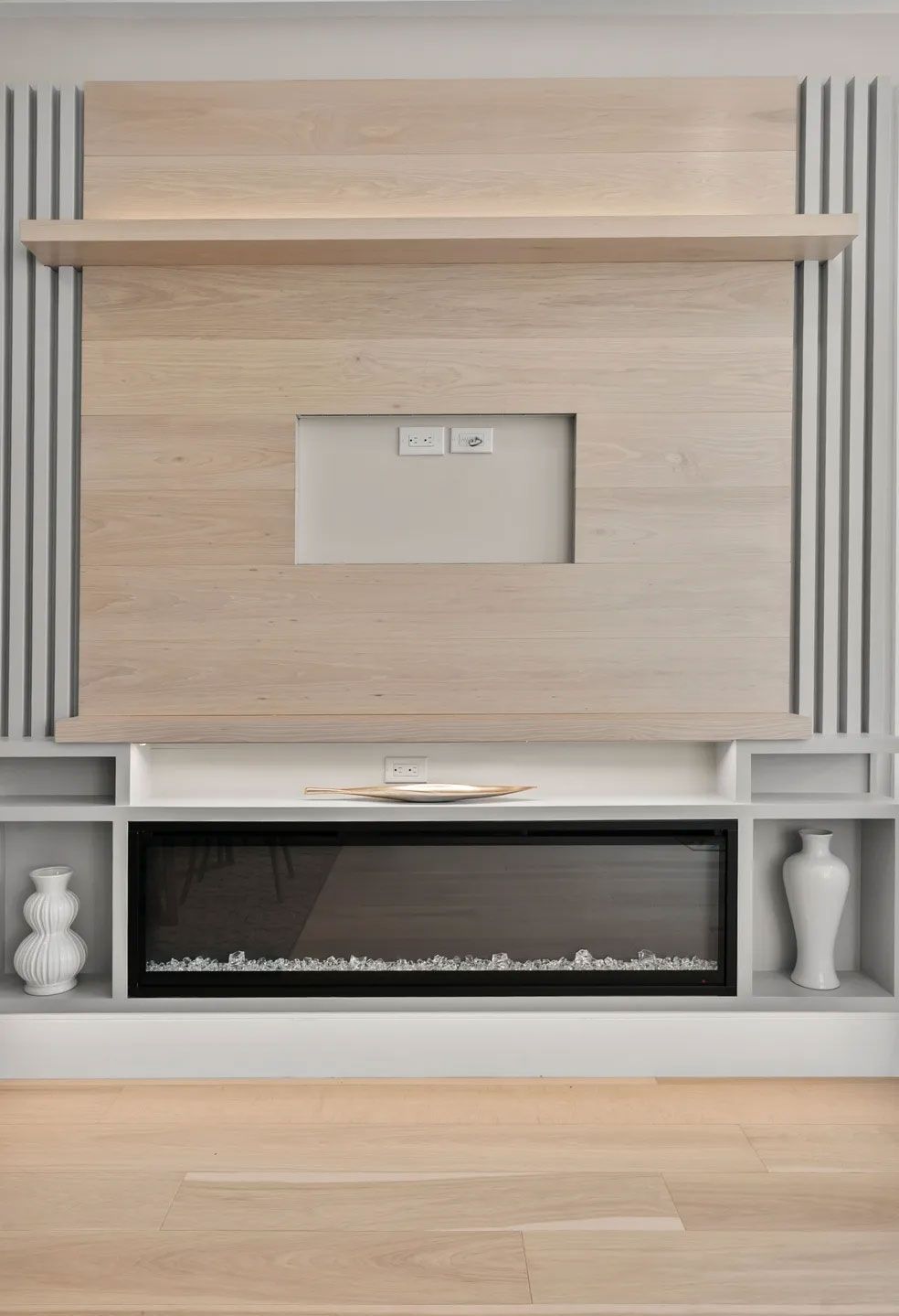 Modern wall unit with fireplace, TV mount, shelves, and vertical wood paneling; light wood tones.