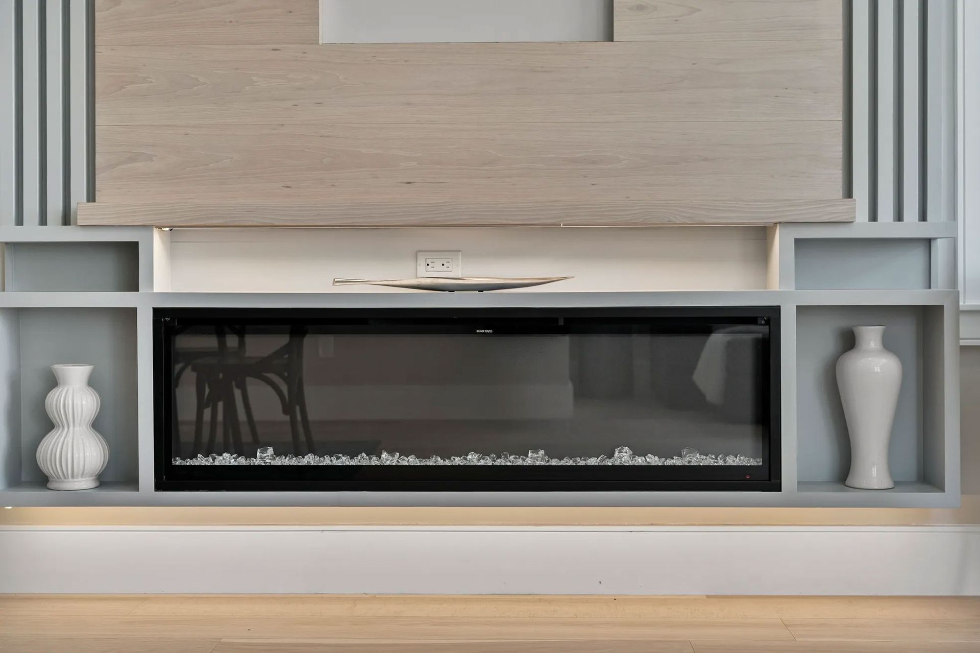 Electric fireplace with a light wood accent above, flanked by gray shelves.