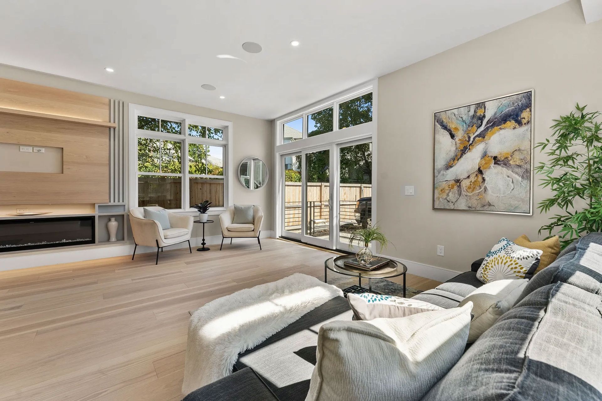 Spacious living room with large windows, light wood floors, and a modern gray sectional sofa.