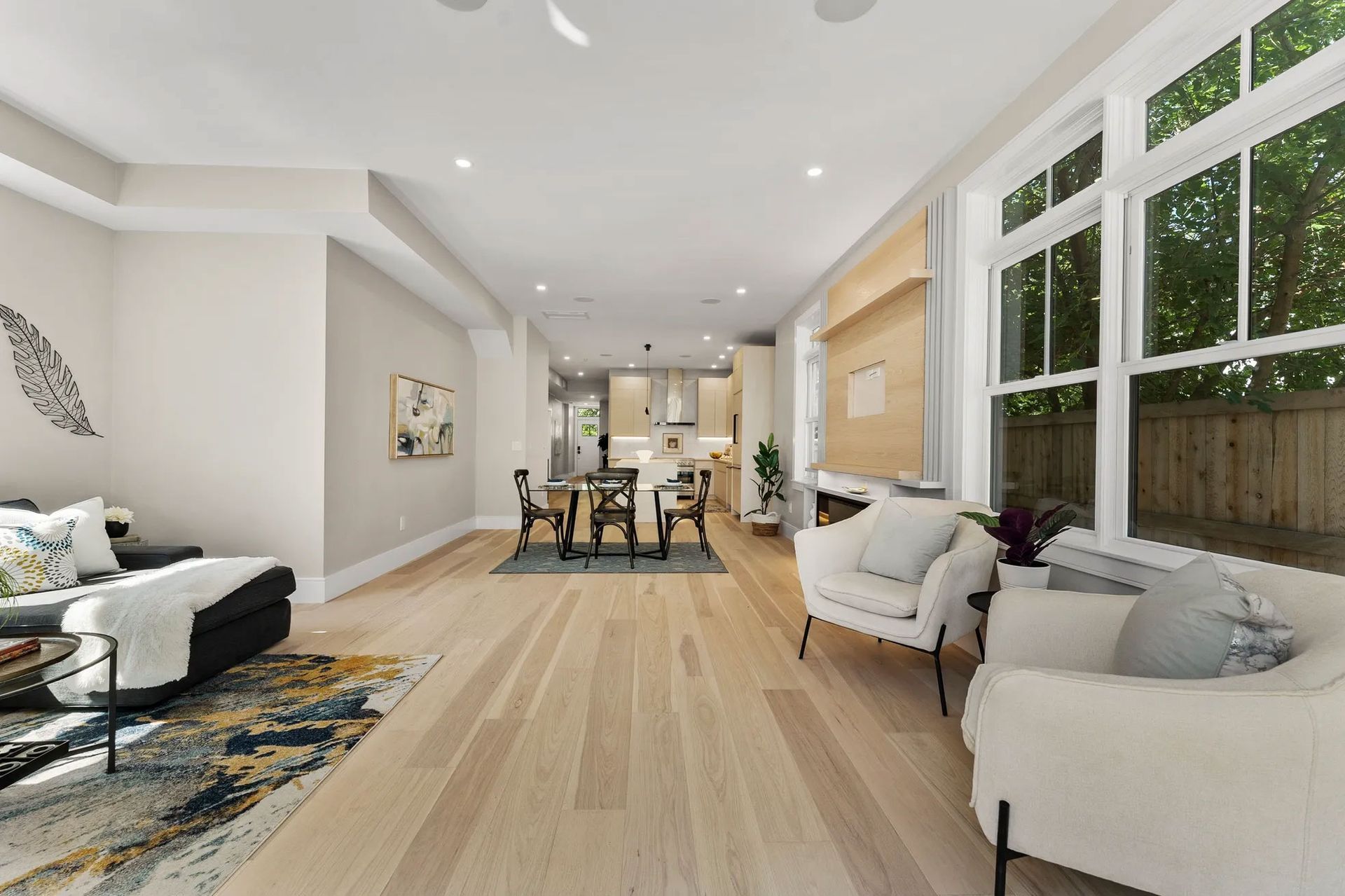 Spacious modern living room with light wood floors, white walls, and large windows.