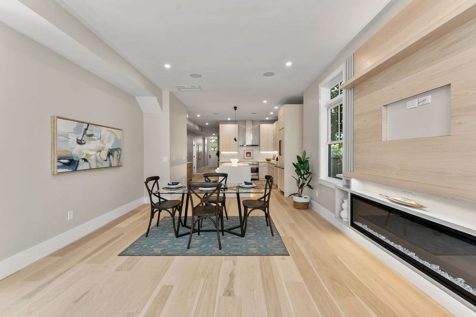 Dining area with table, chairs, and art, leading to a kitchen with a fireplace on the right.